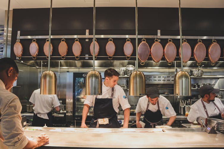 A line of chefs wearing black aprons at work in an open kitchen.